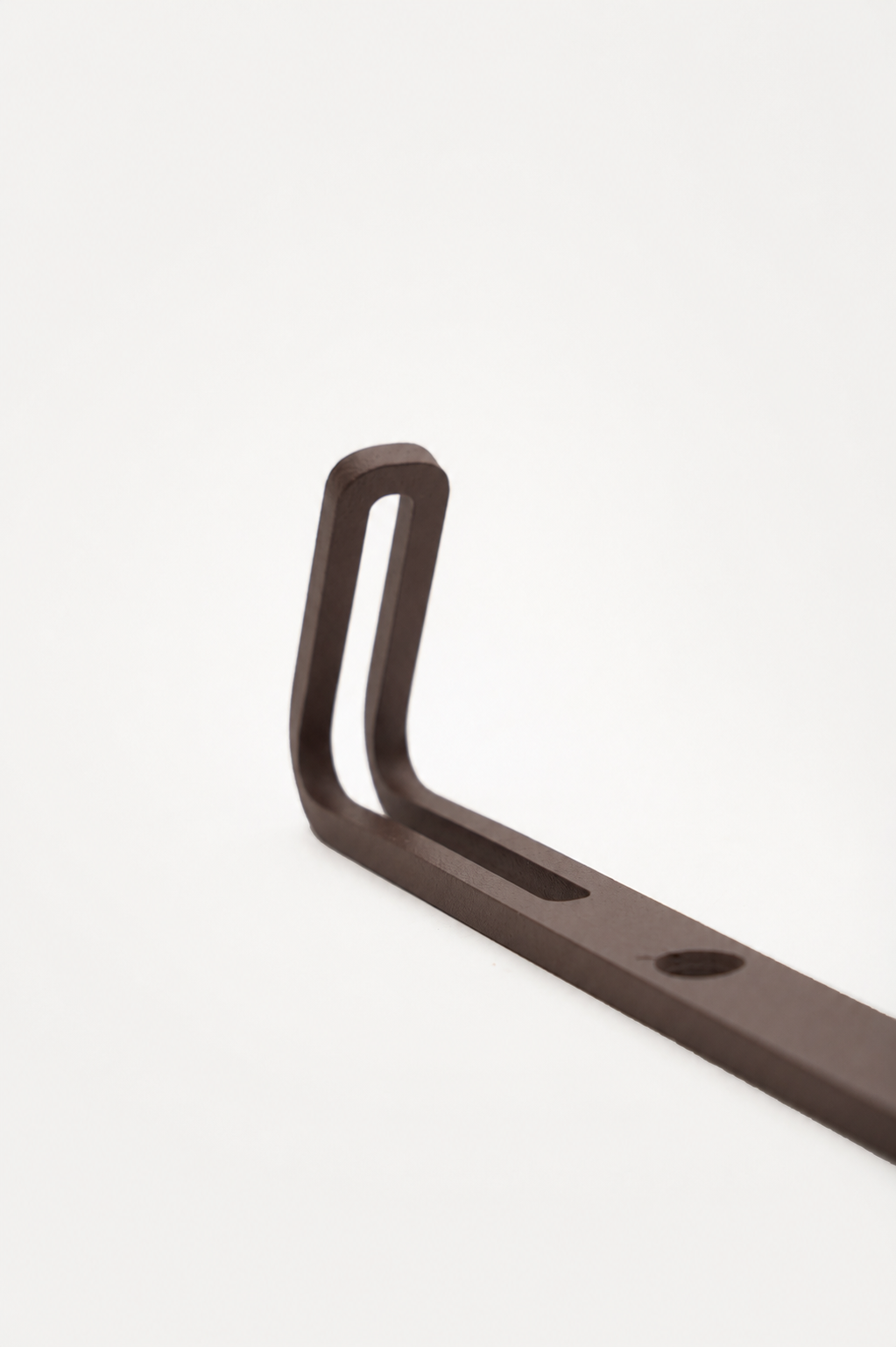 AIKI wall hook in Umber powder coated steel, RAL 8022, macro of the forked prong top and slotted bracket, dark black brown