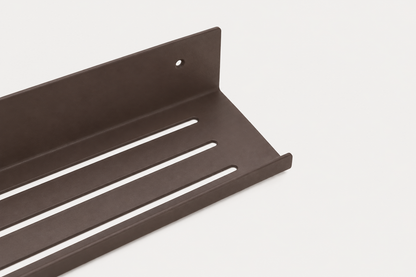 ELIORA shower shelf in powder coated steel, wide close-up of the slotted tray in dark chocolate brown, screw hole at the right