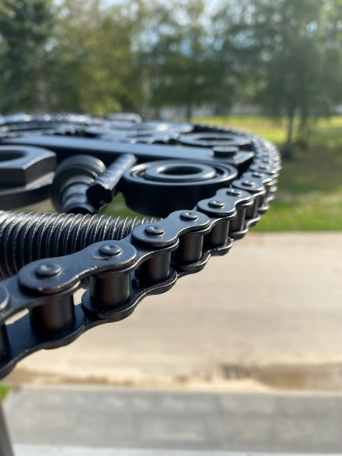 Close-up of a one-off ATYP piece welded from bicycle chains, gears, and springs, powder coated black.