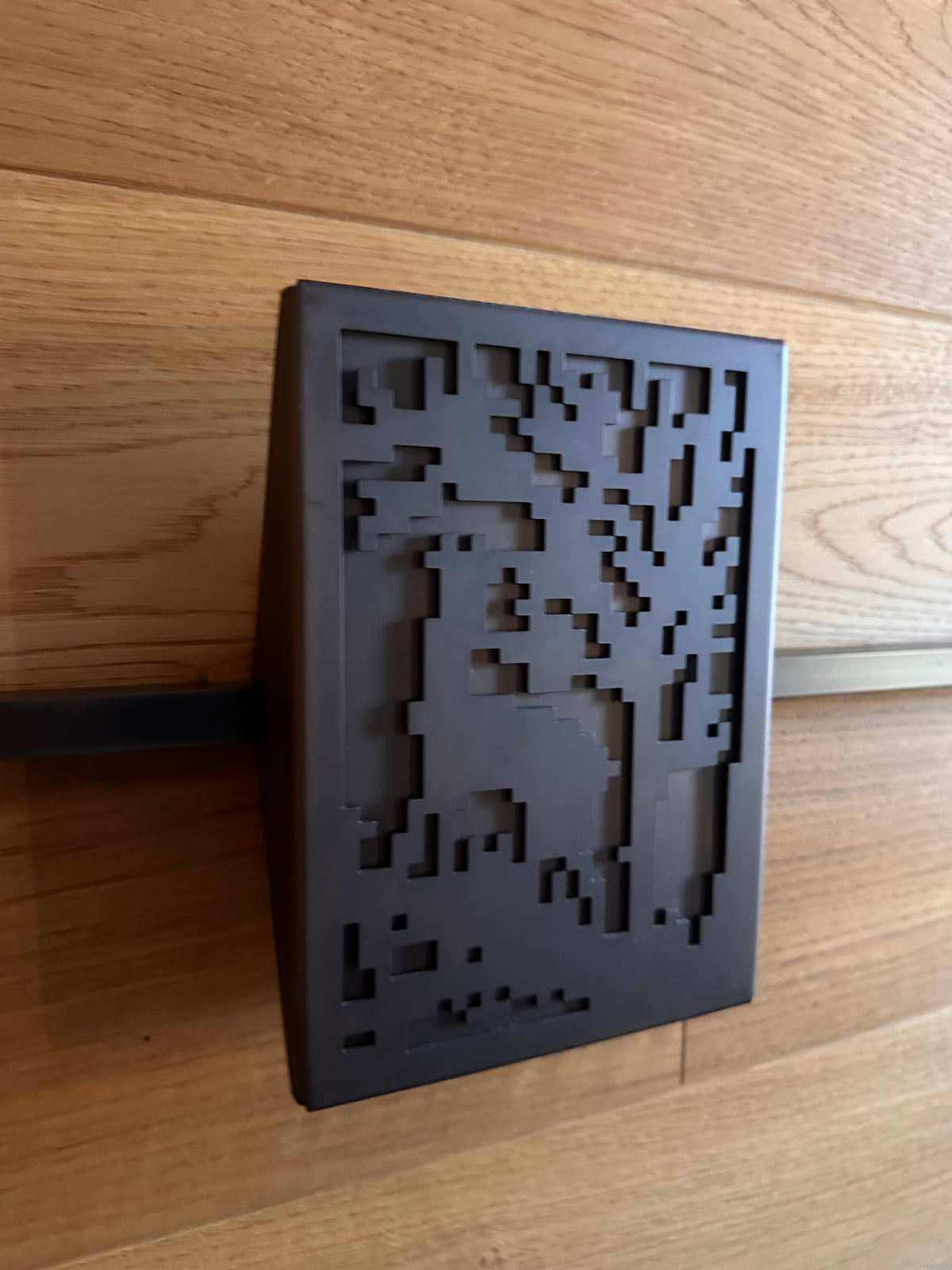 A custom ATYP steel wall panel with a pixel style tree motif, powder coated dark brown, mounted on an oak slat wall.