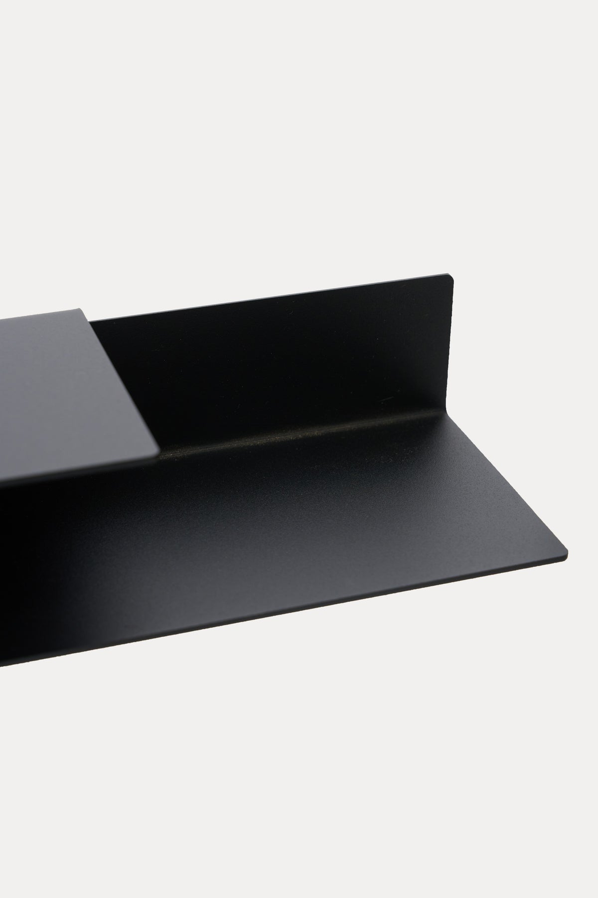 NYVE toilet paper holder in powder coated steel, wide close-up of the shelf and hook arm with roll slot, deep black with a soft sheen